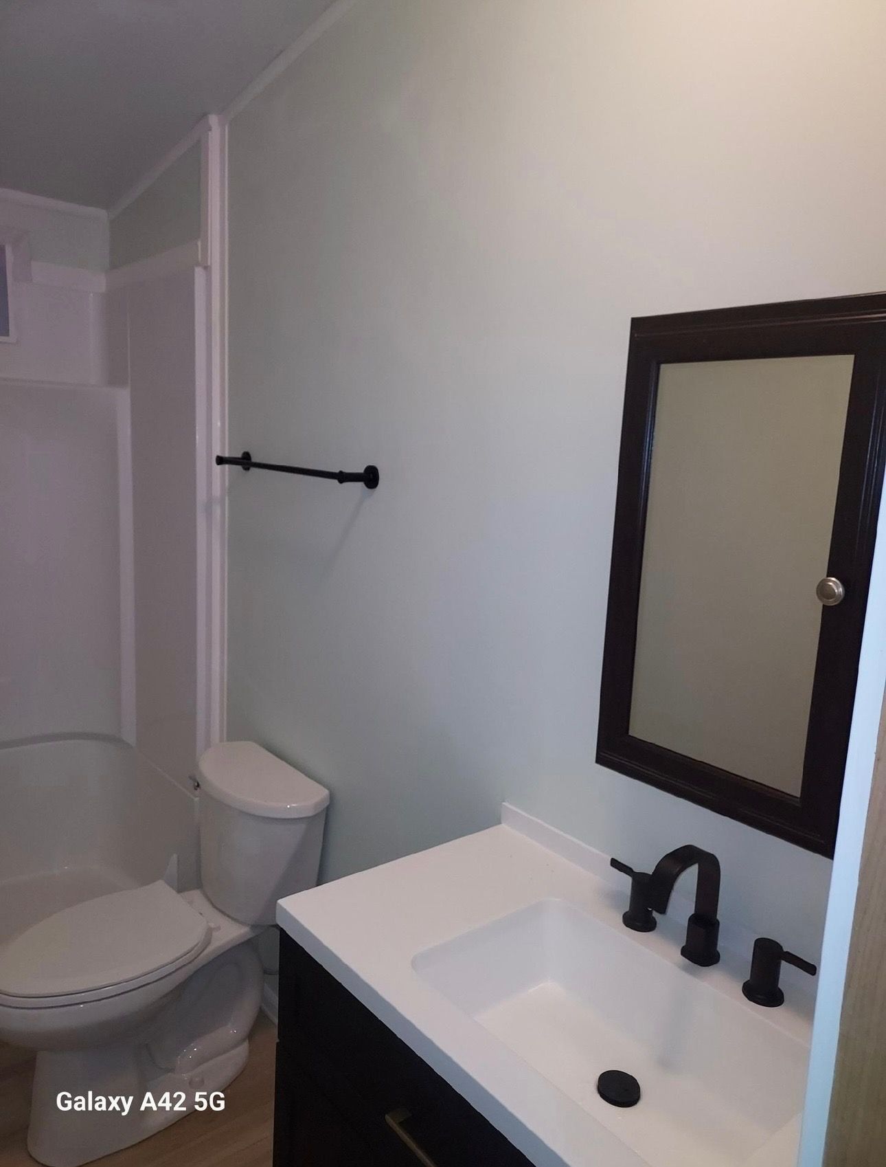 A modern bathroom featuring a white vanity with black hardware, a black-framed mirror, a toilet, and a shower stall.