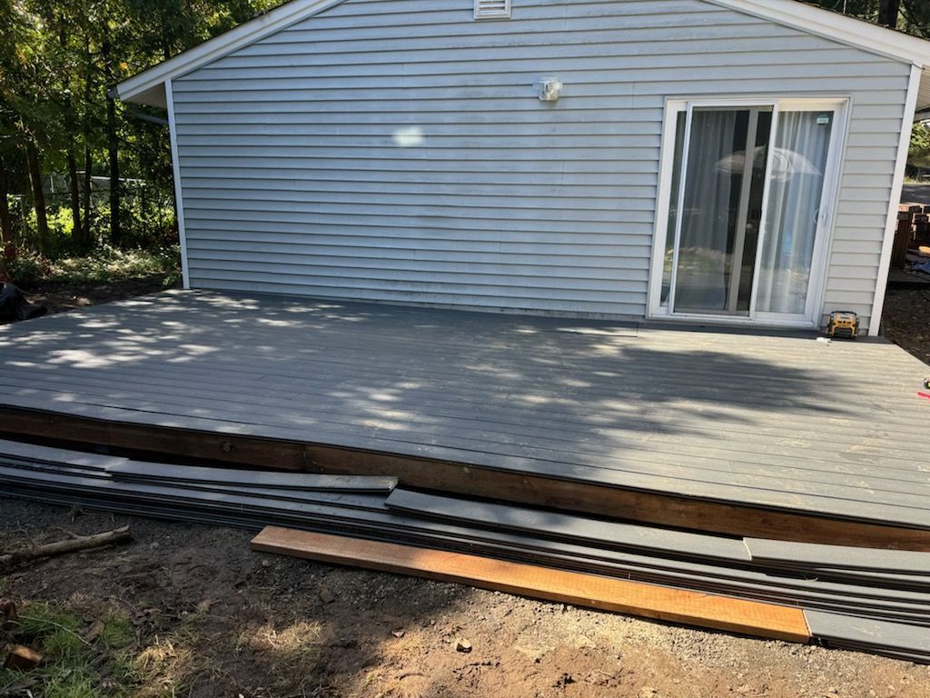 A newly installed gray composite deck outside the back of a light gray vinyl-sided house with a sliding glass door.