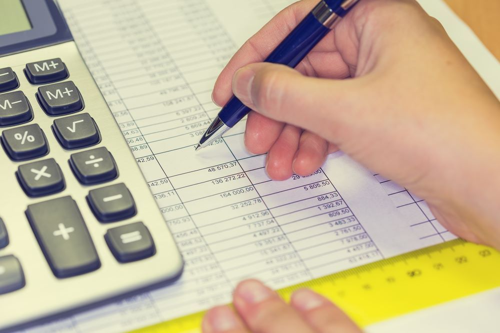 A Person is Writing on a Piece of Paper Next to a Calculator — Repo Busters Wyong In Wollongong, NSW