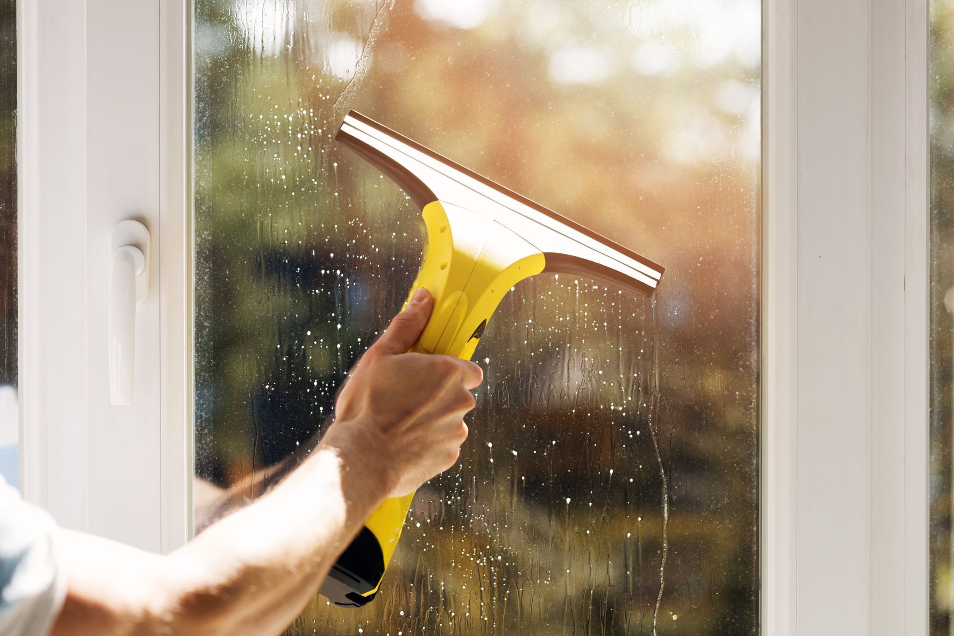 A close-up of a person cleaning a window with a yellow window cleaner