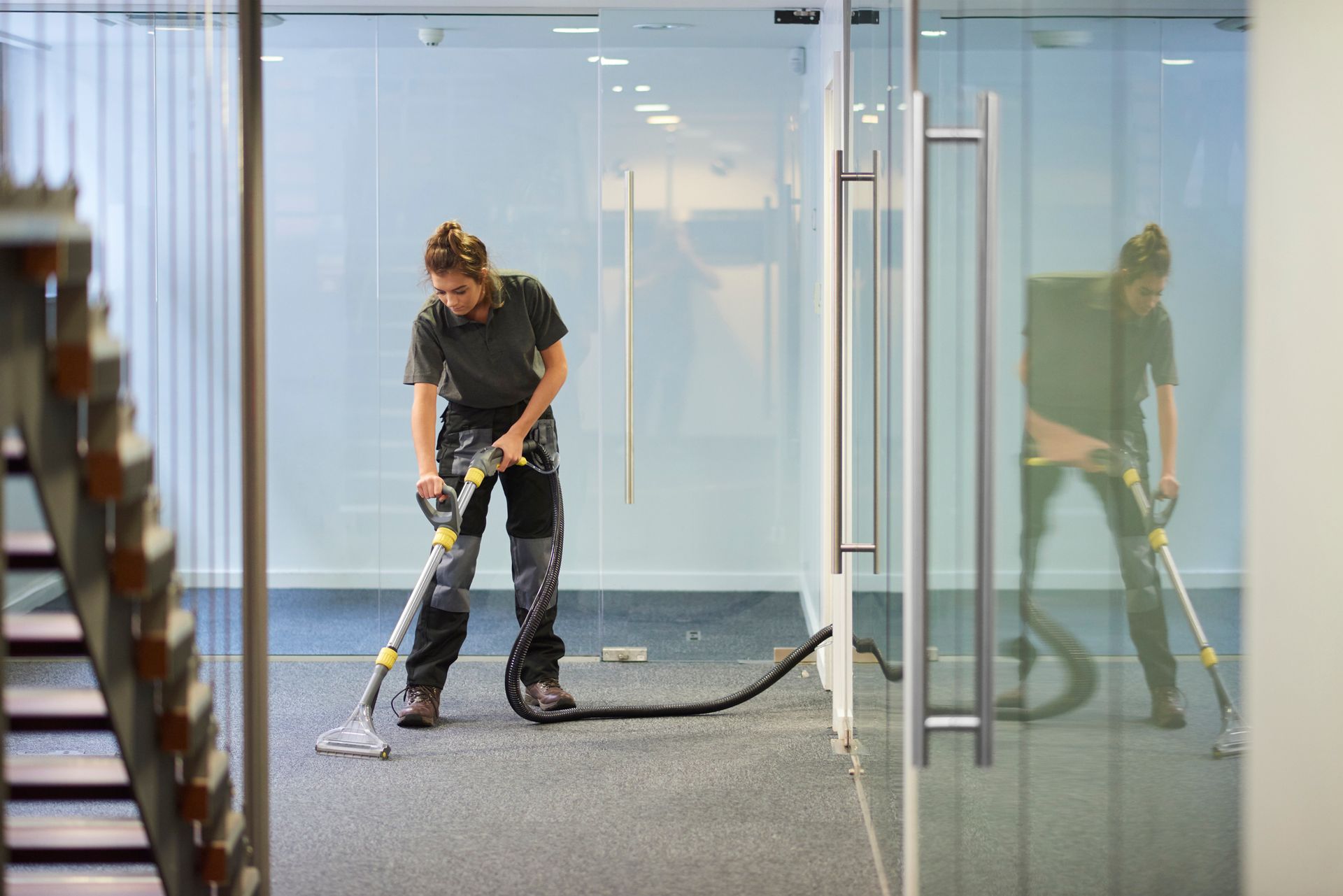 Woman using vacuum cleaner on carpet in office.