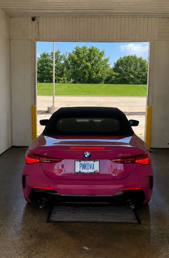 Red BMW convertible parked inside a garage, facing an open doorway with green trees outside.
