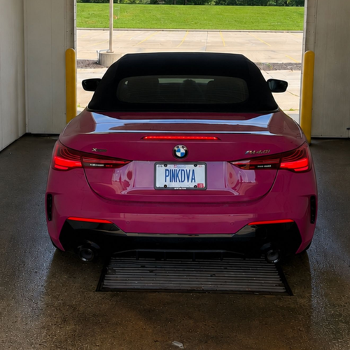 Red BMW convertible parked inside a garage, facing an open doorway with green trees outside.
