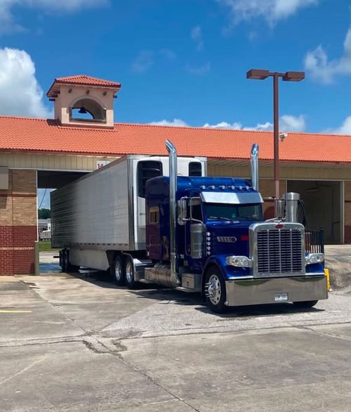 Blue semi-truck parked outside a building under a bright blue sky