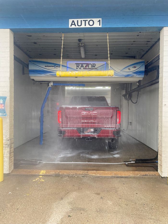 Red pickup truck in an automatic car wash bay, spraying water and foam.