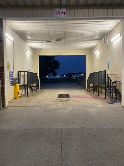 Empty car wash bay at night, with bright overhead lights and an open view outside.
