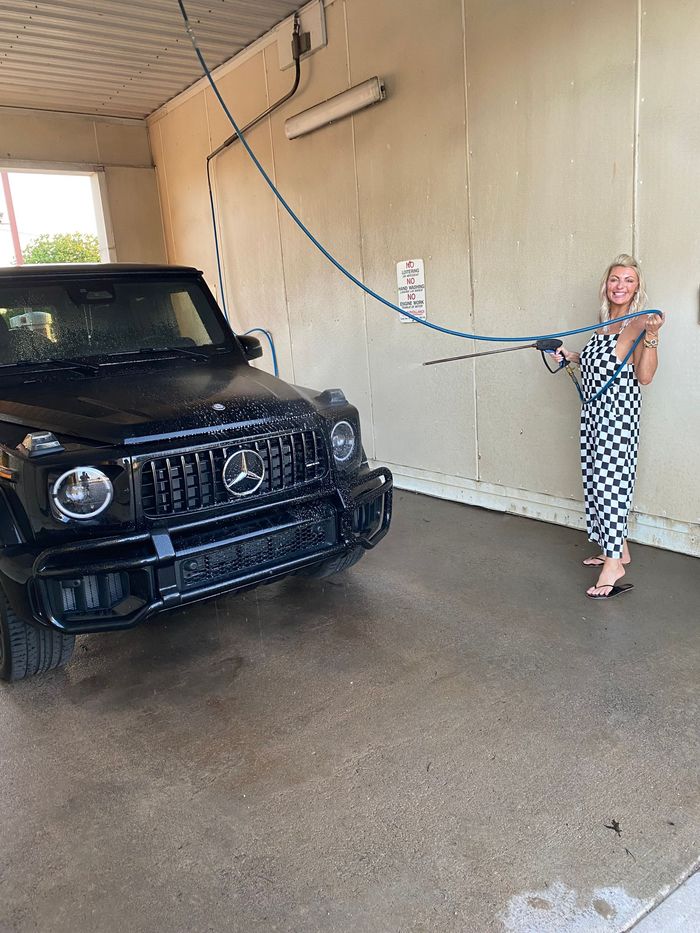 Woman holding a hose beside a black SUV in an indoor car wash bay