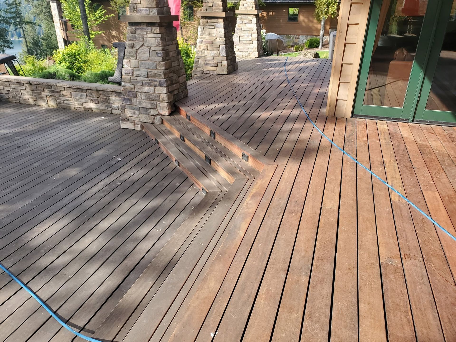 Wooden deck with stone pillars, slatted shadows, and a blue rope under a covered outdoor patio.