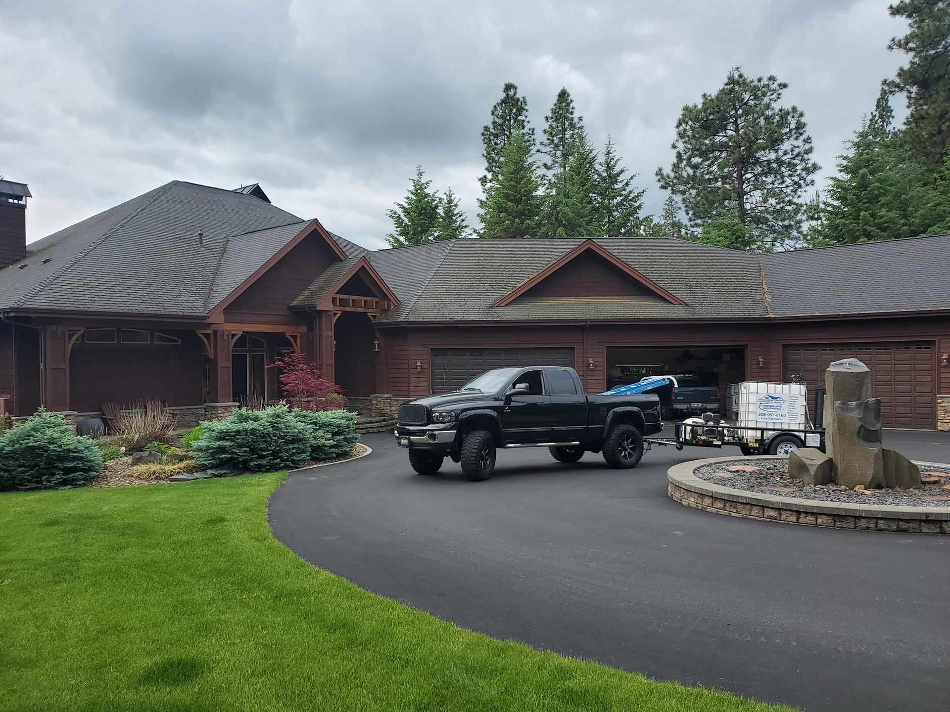 Wooden house with dark roof, black pickup truck, and curved driveway under cloudy sky