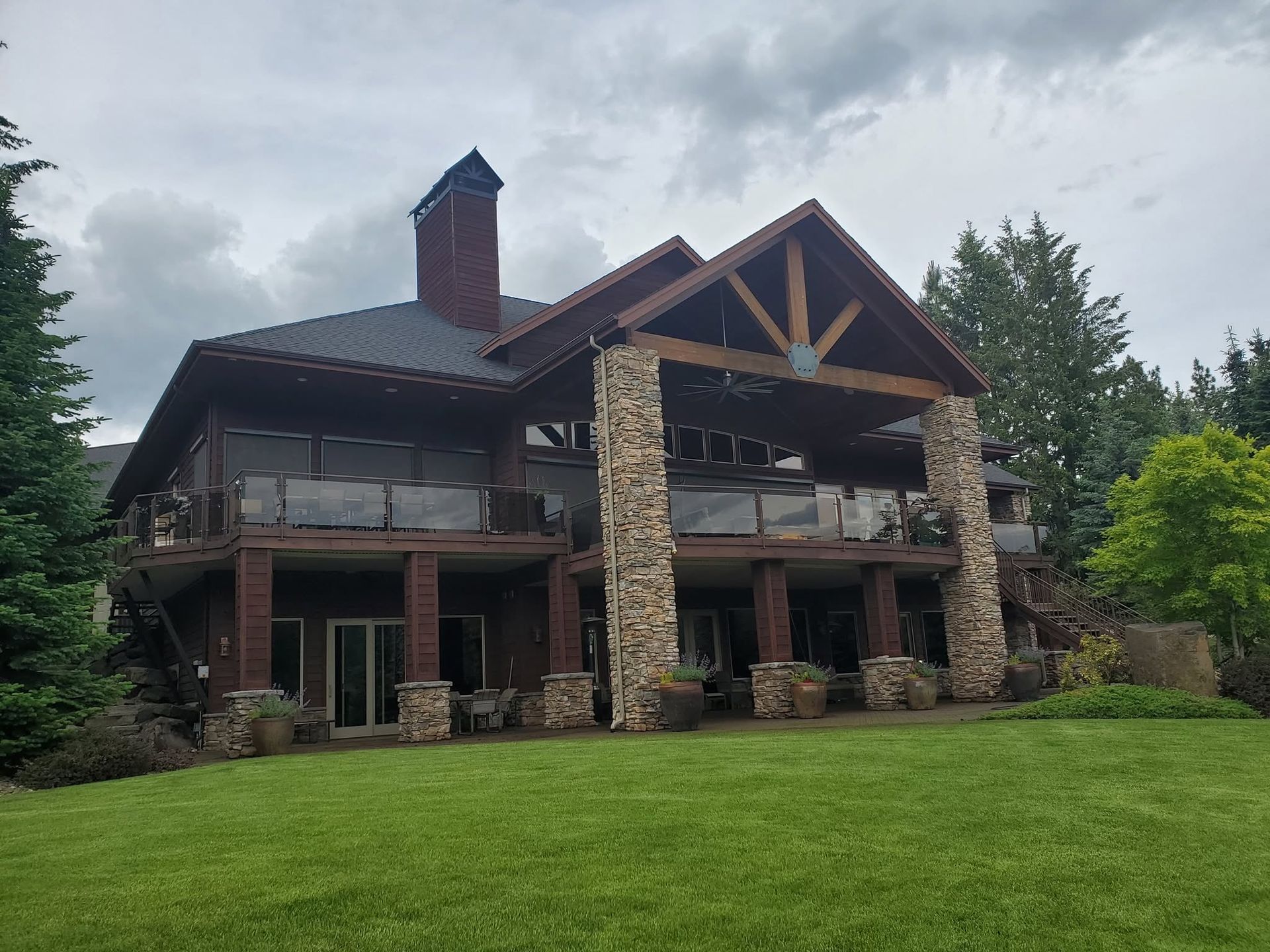 Large rustic lodge with stone pillars and a covered porch on a green lawn under cloudy sky