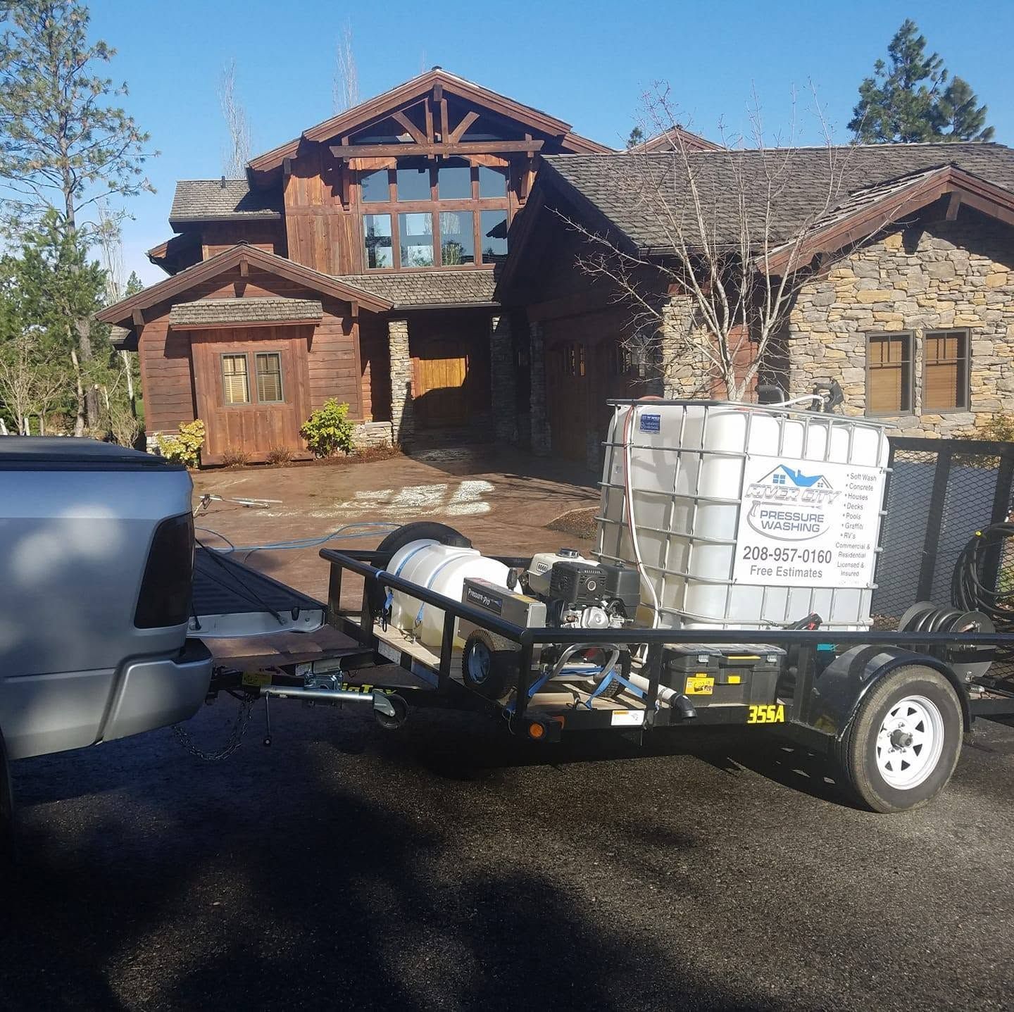 Pickup truck towing a utility trailer with a white tank in front of a rustic stone house.