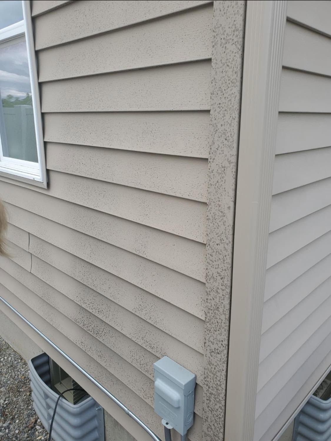 House siding corner with two utility boxes and a basement vent near the foundation
