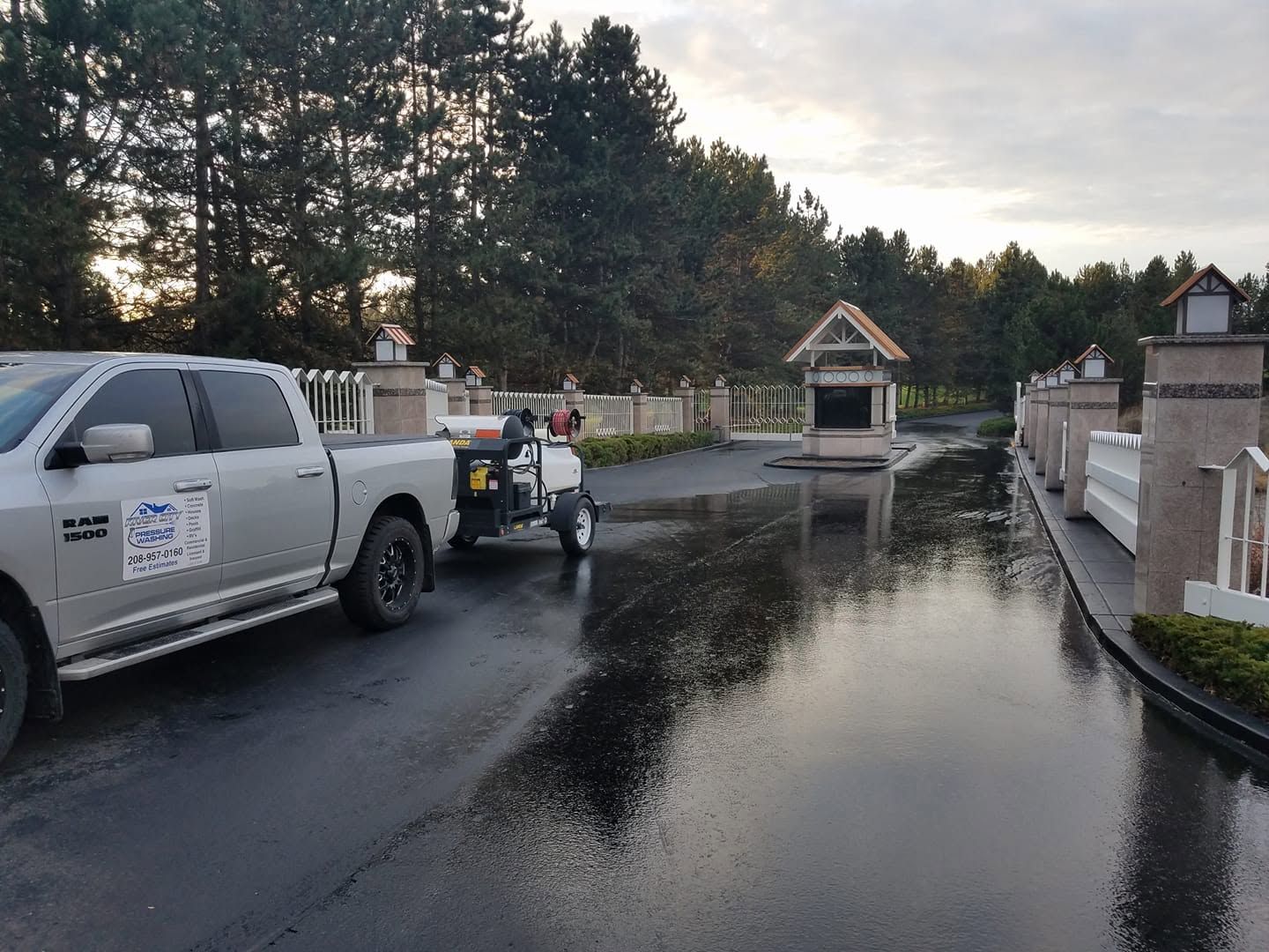White pickup towing equipment on a wet driveway near a gated entrance at dusk