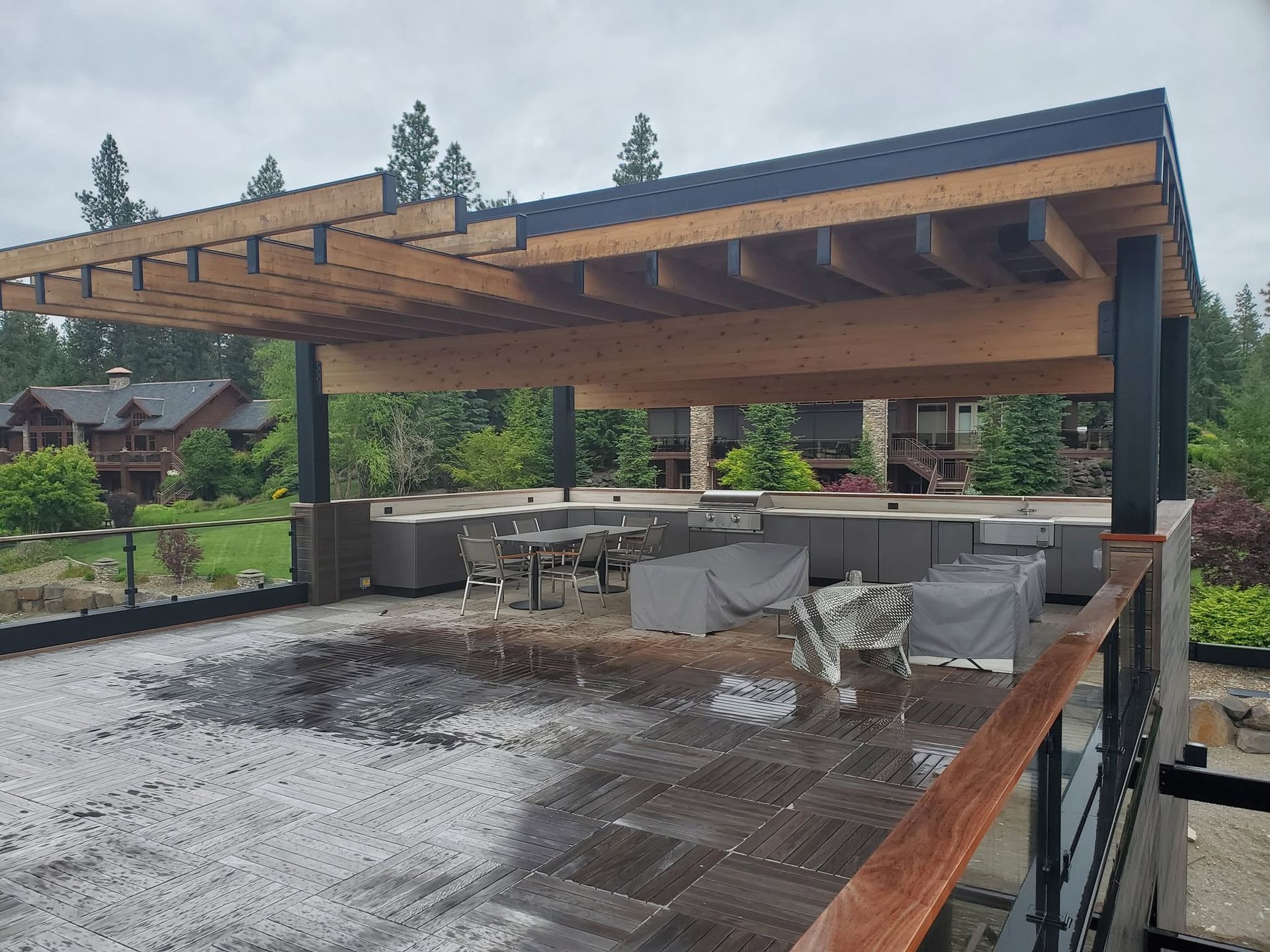 Covered outdoor patio with wooden pergola, tables, and chairs overlooking a wet rooftop or terrace.