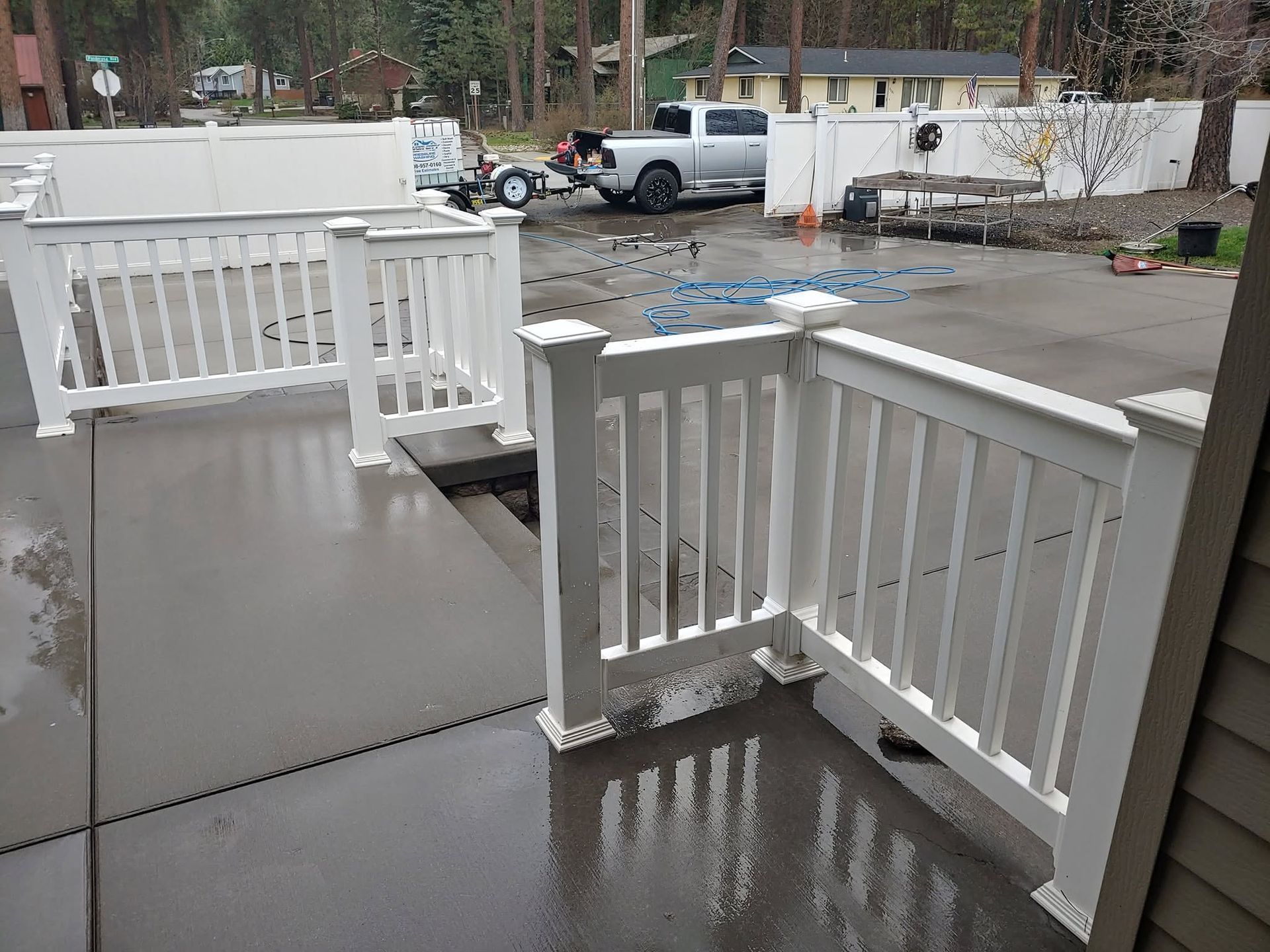Rainy porch with white railings and steps overlooking a wet parking lot and cars in the background