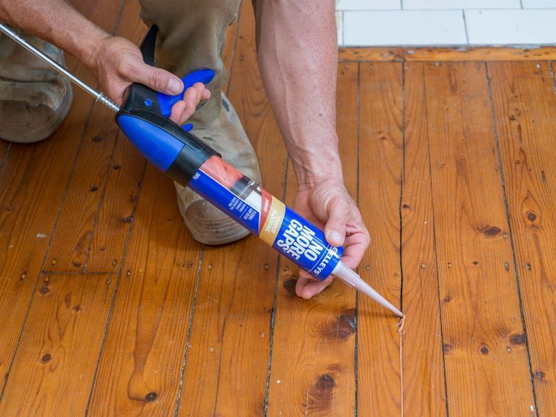 Person applying blue sealant to a wooden floor with a caulking gun