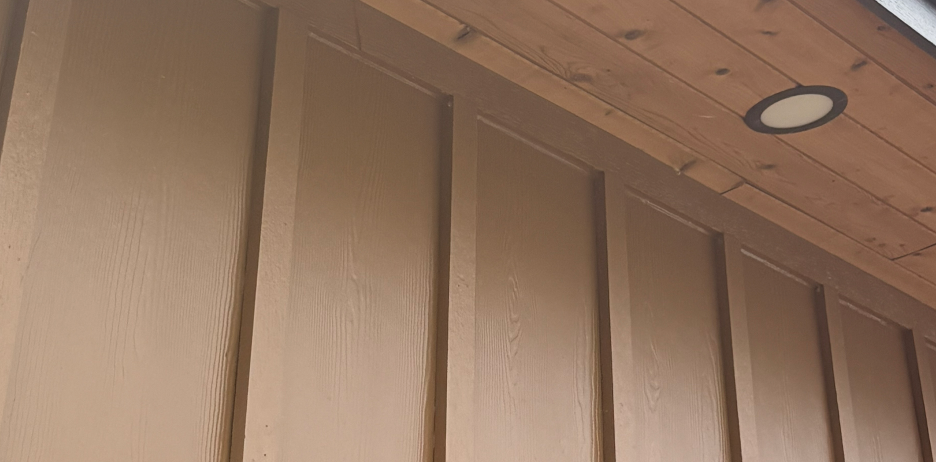Wood-paneled wall and ceiling with a recessed light in a cozy interior corner