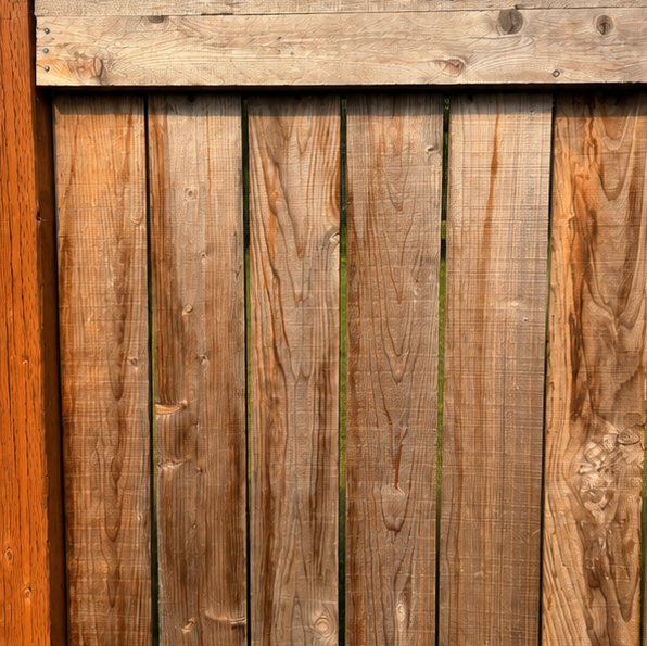 Close-up of a weathered wooden fence with vertical brown planks and a horizontal top board.