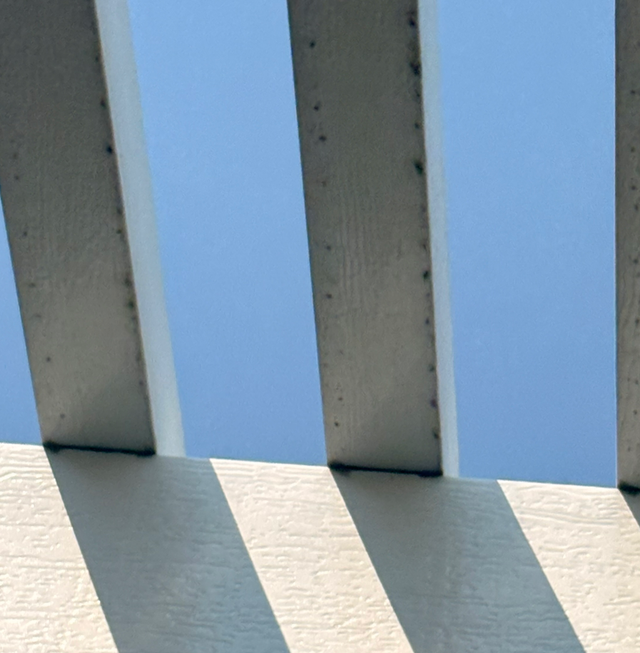 White beams casting long shadows on a blue sky above a light-colored wall