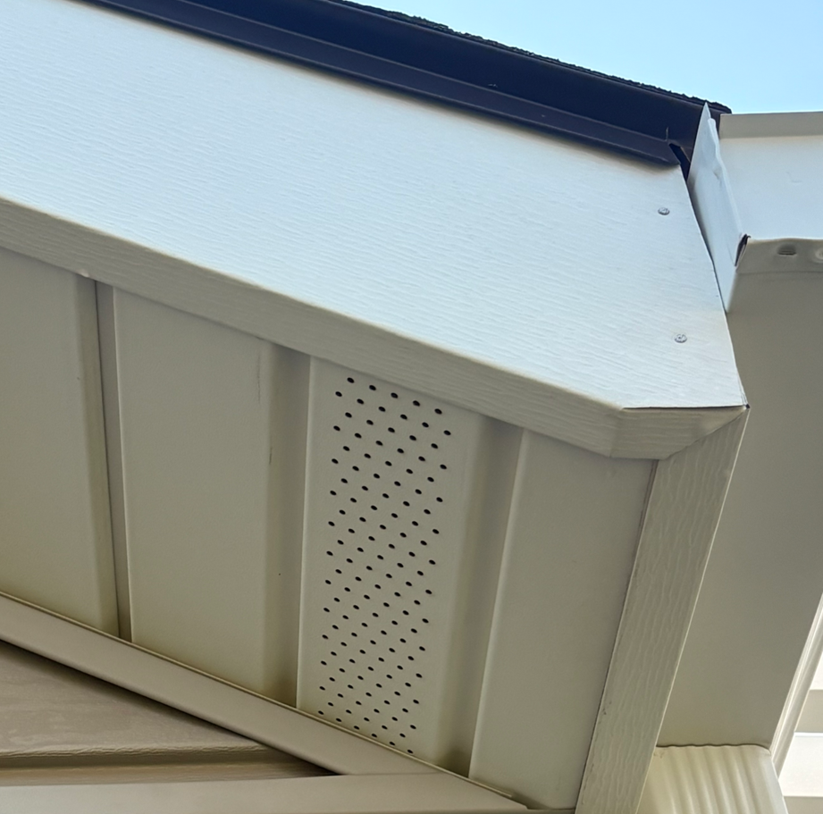 White soffit and vented eaves beneath a dark roof against a blue sky
