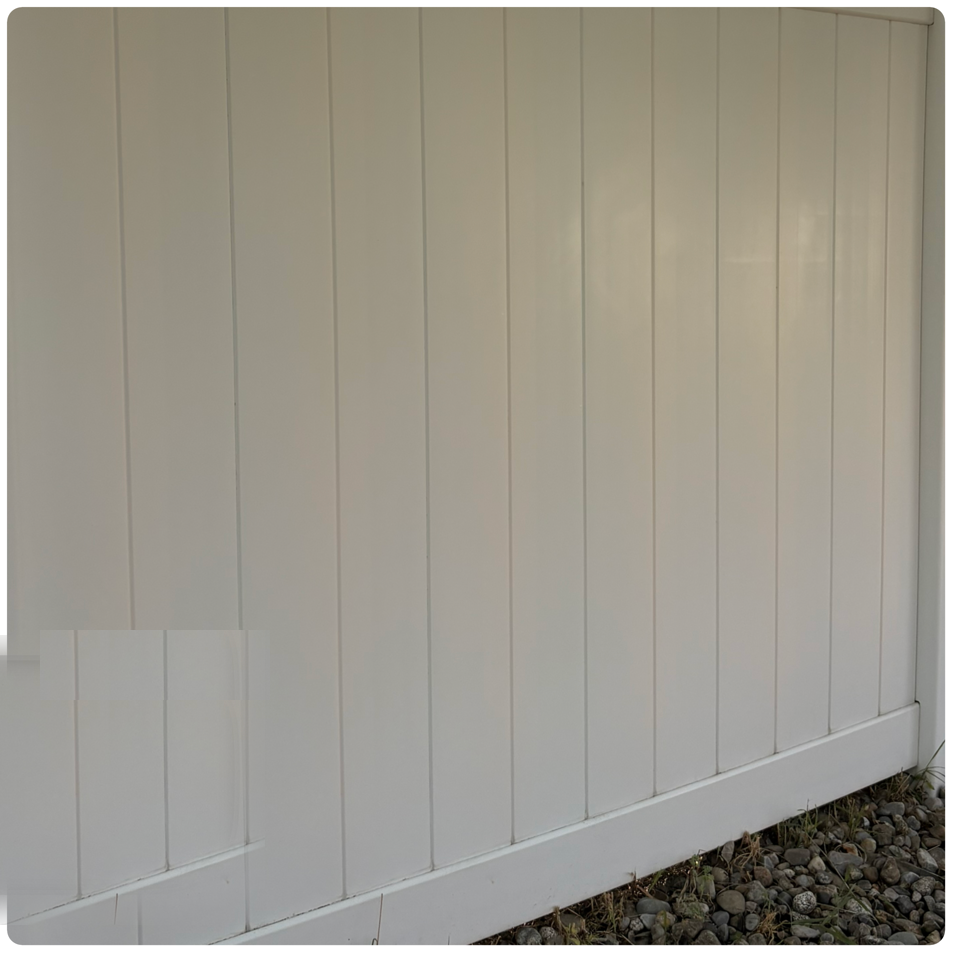 White vertical-paneled fence or wall with a diagonal base above gravel