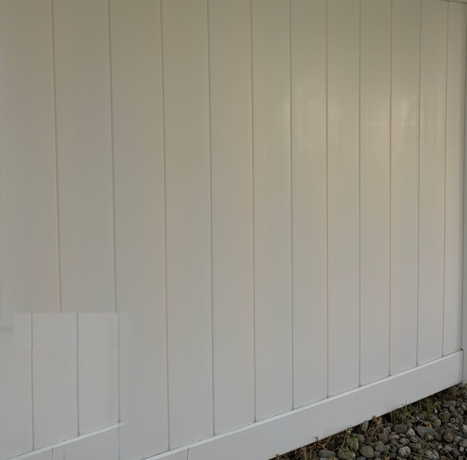 White vertical-paneled fence or wall with a diagonal base above gravel