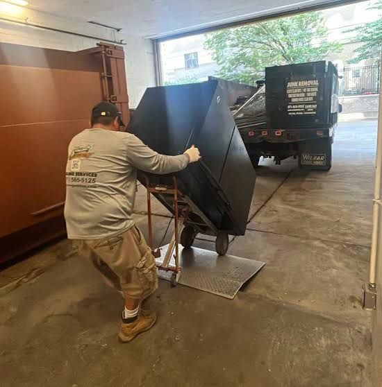 Worker pushing a large black object on a hand truck toward a truck in a garage loading area.
