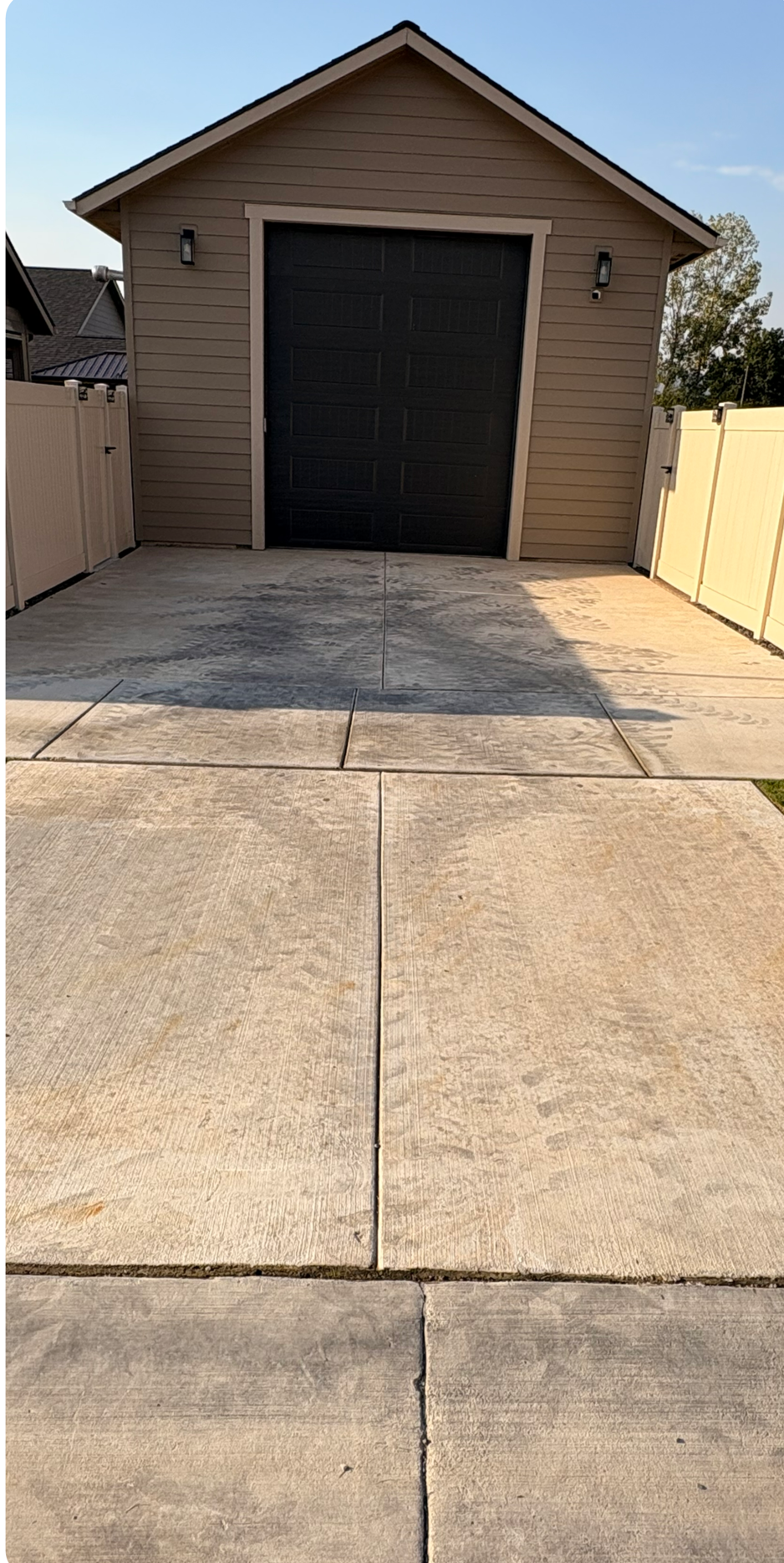 Concrete driveway leading to a tan garage with a black door and blue sky overhead