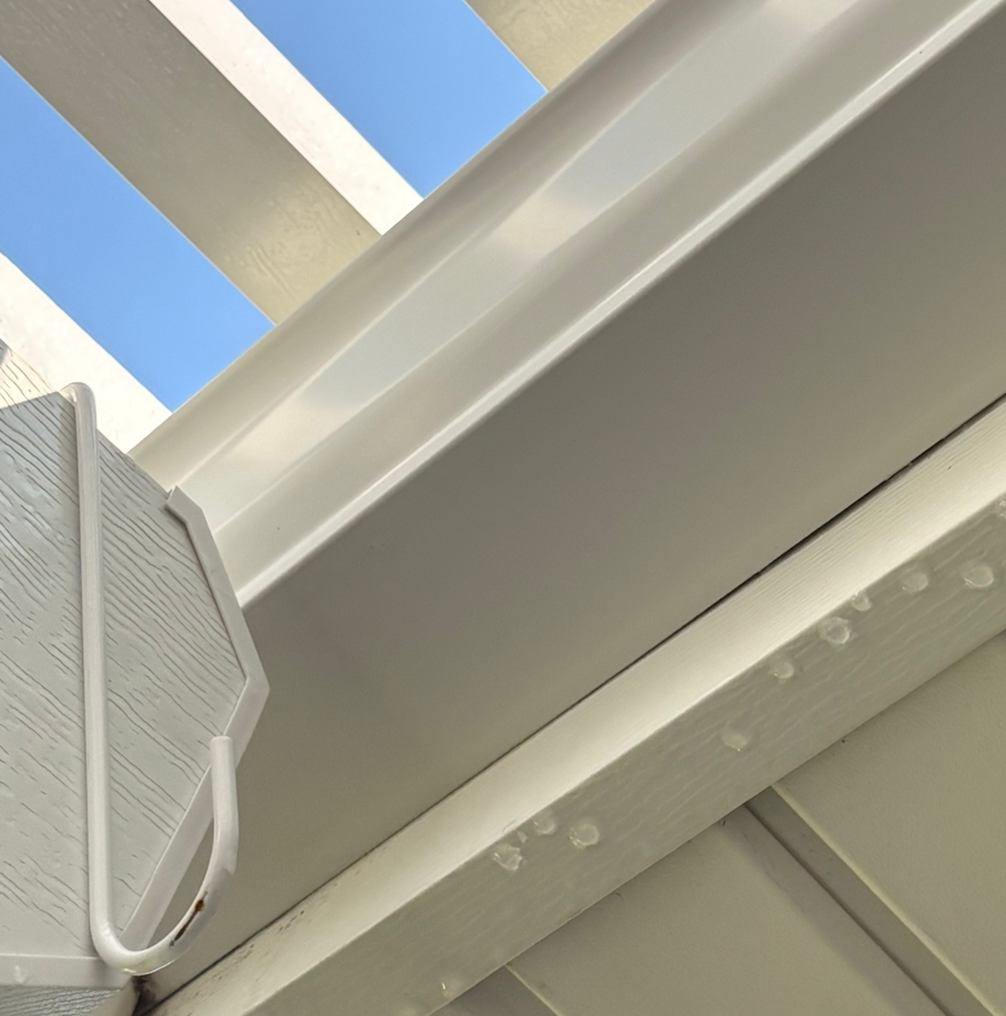 Close-up of a white window shade and track beneath a slanted skylight with blue sky visible