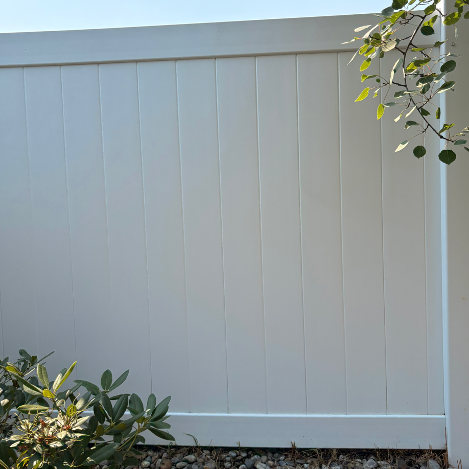White vinyl fence in a garden with green leaves and plants along the bottom and right edges