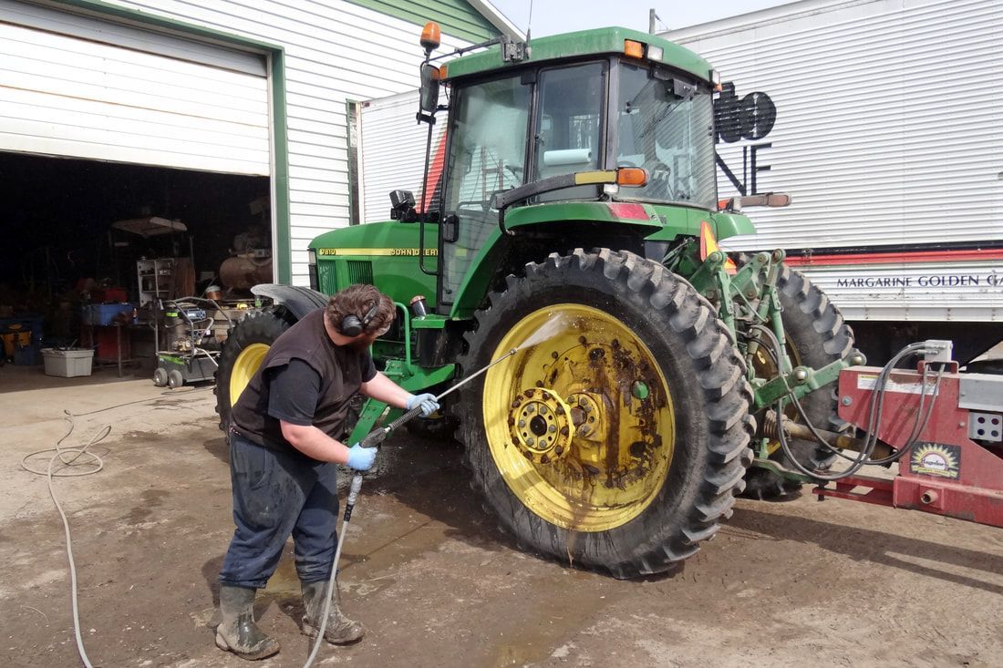 Tractor spraying water on green crop rows as two workers stand in a muddy field