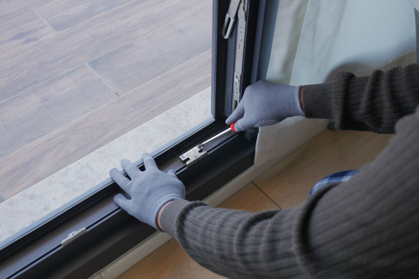 Gloved hands adjusting a sliding door track beside a wood floor and glass door