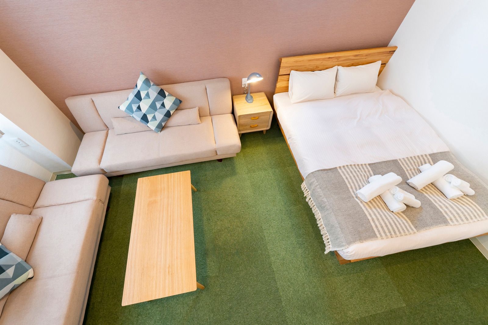 Cozy bedroom with bed, sofa, floor mat, and green carpet in a small, bright room