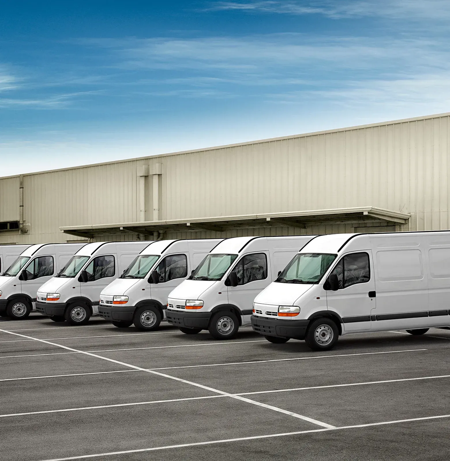White cargo vans parked in a row outside a warehouse on a paved lot