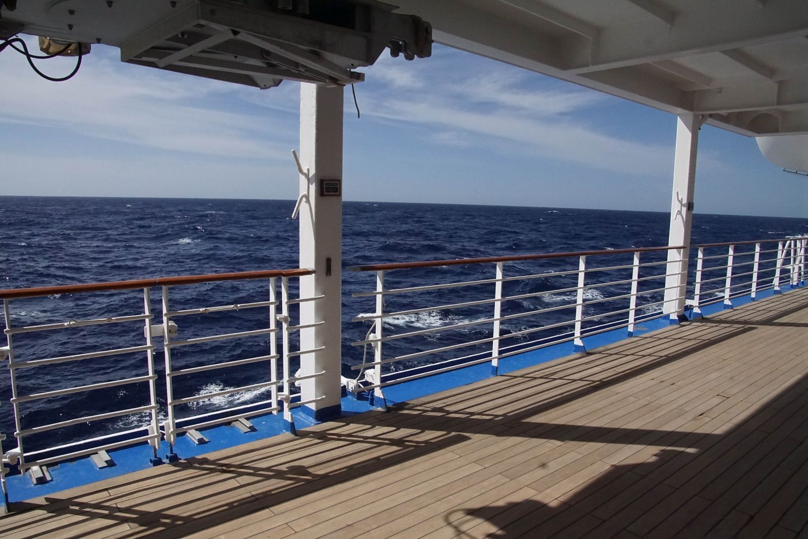 Ship deck overlooking the open ocean with blue water and white railings under a clear sky