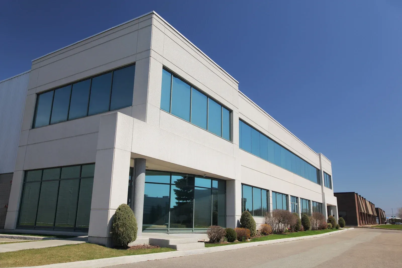 Modern two-story white office building with blue-tinted windows on a sunny day