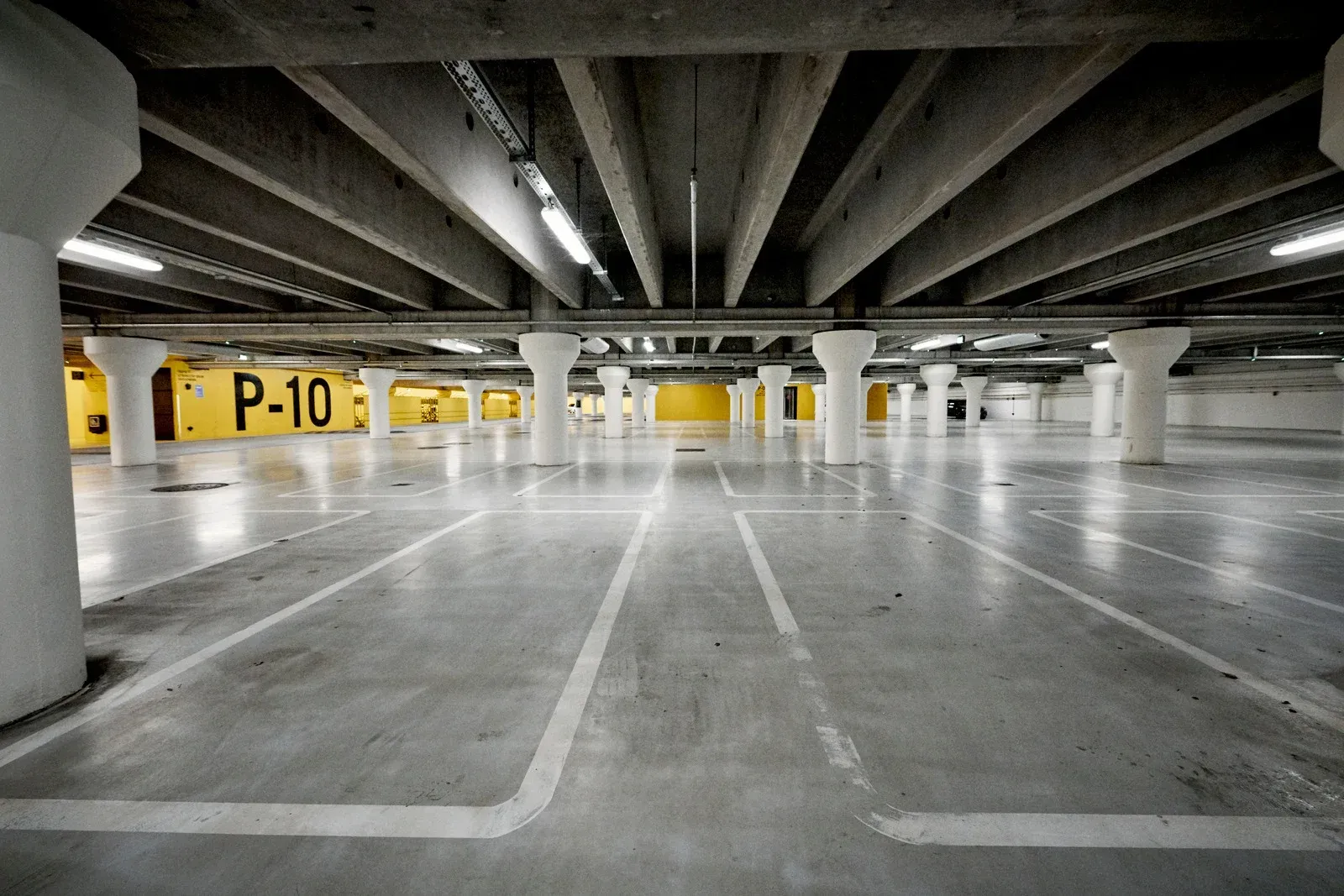 Empty parking garage with concrete pillars, overhead lights, and yellow P-10 signs.