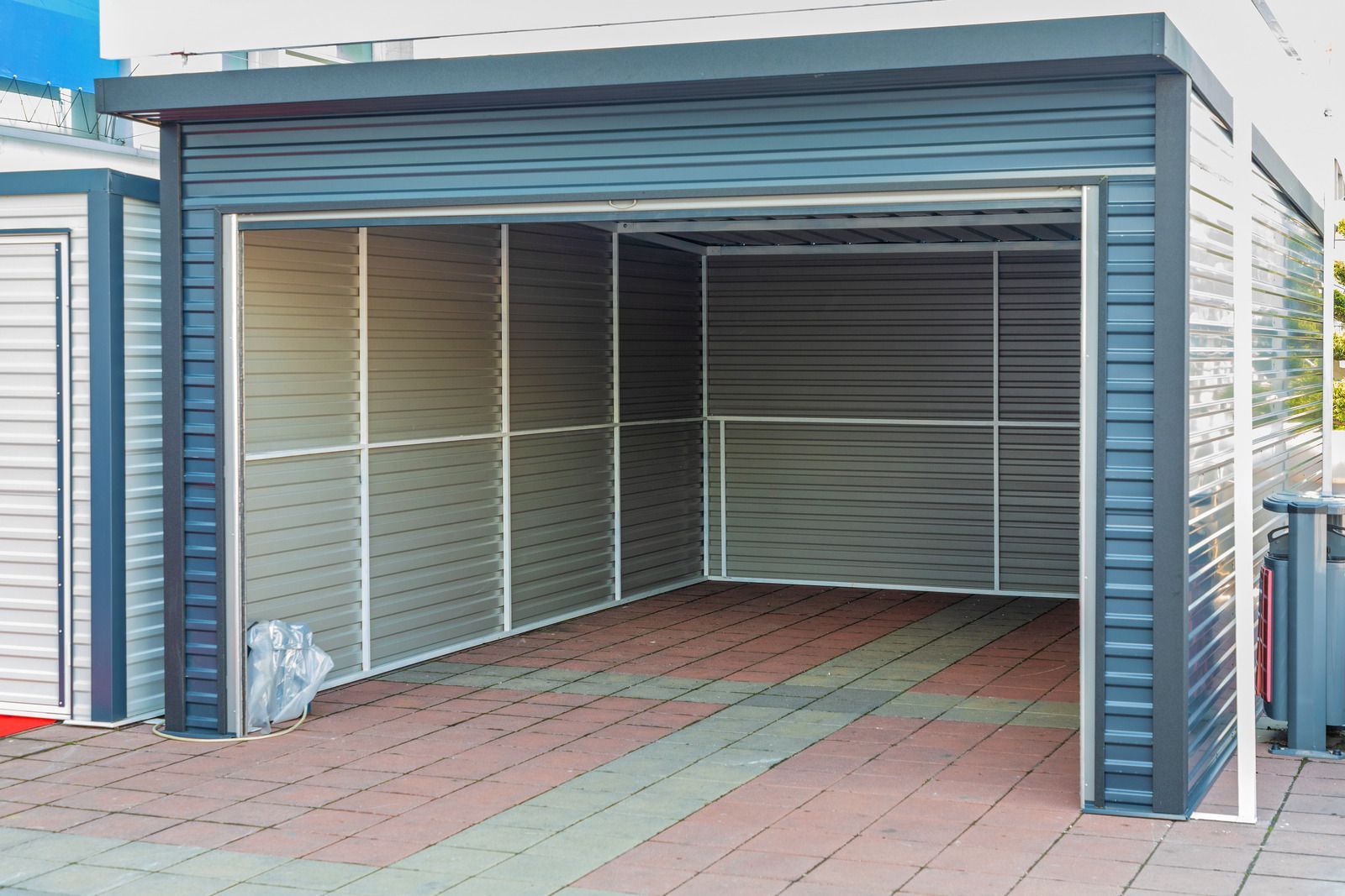 Open metal garage with blue trim and red paver floor, viewed from the front