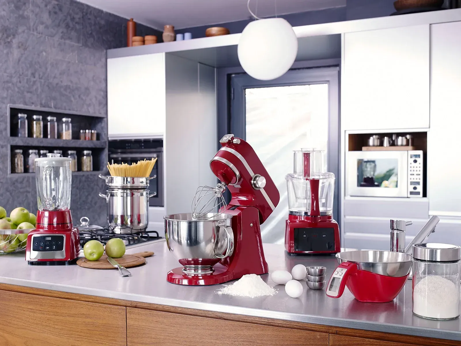 Kitchen counter with several red and stainless-steel appliances, fruit, and white dishes in a bright modern room