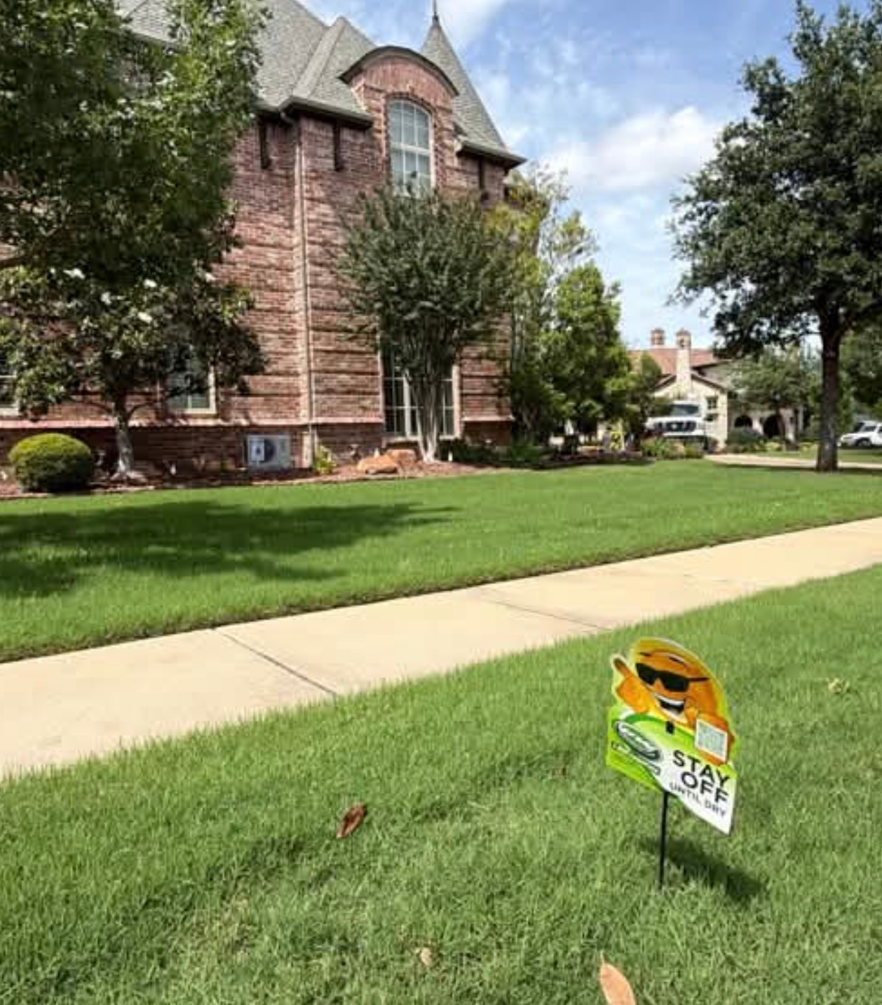 Brick Colleyville home with a front lawn, stone walkway, and a small yard sign by the entrance.