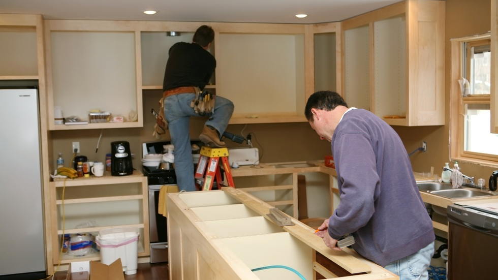 Two people installing cabinets in a kitchen under renovation.