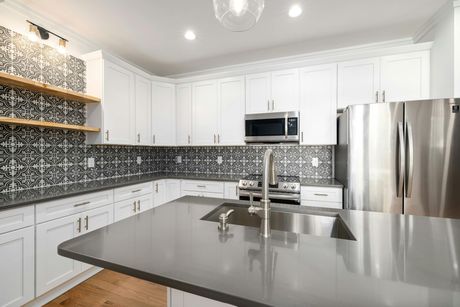 A modern kitchen with white cabinets, gray quartz countertops, stainless steel appliances, and black patterned tile.