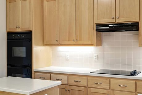 A kitchen featuring light wood cabinets, white countertops, a black wall oven, and a black cooktop with a range hood.