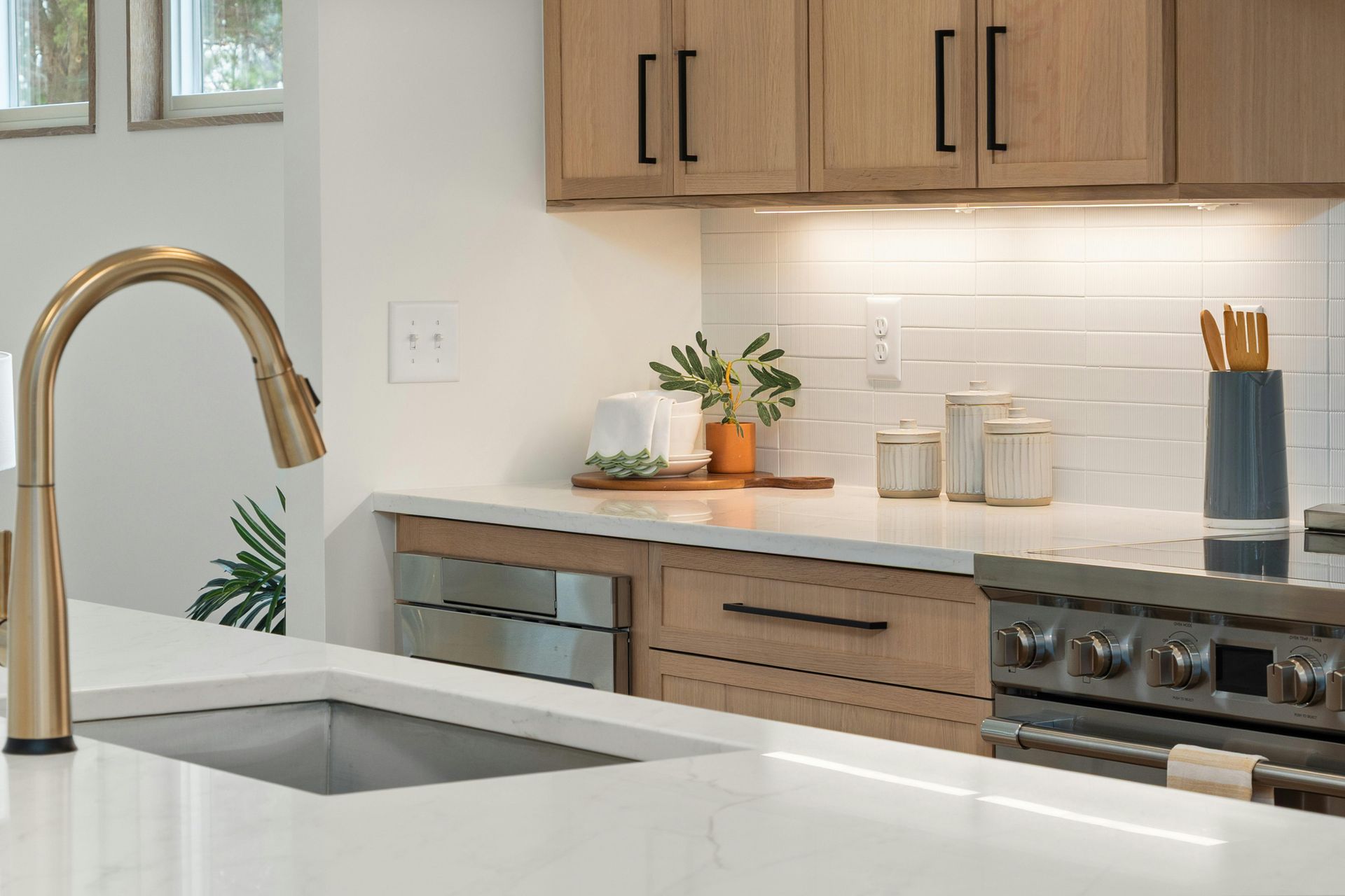 A modern kitchen with light wood cabinets, white marble countertops, a gold faucet, and a subway tile backsplash.