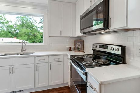 A bright kitchen with white shaker cabinets, white countertops, a stainless steel microwave, and a subway tile backsplash.