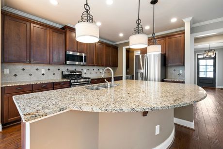 A kitchen features dark wooden cabinets, granite countertops, a large curved island, and three pendant lights.