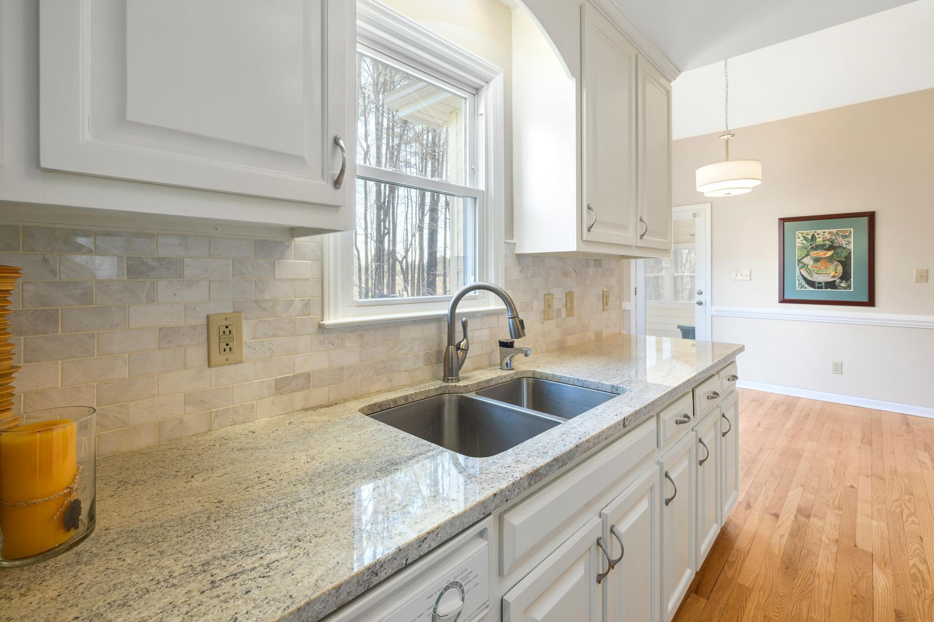 A bright kitchen featuring white cabinets, granite countertops, a stainless steel sink, and a tiled backsplash.