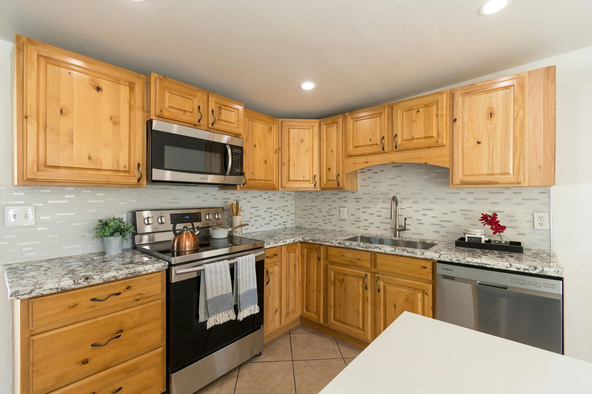 A kitchen featuring honey-colored wooden cabinets, speckled granite countertops, stainless steel appliances, and tile.