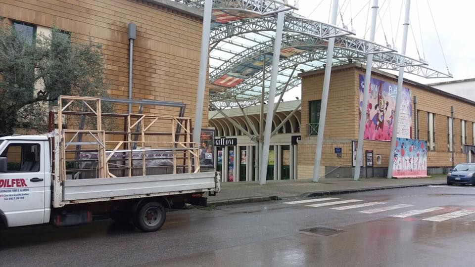Un camion bianco parcheggiato su una strada bagnata di fronte a un edificio color marrone chiaro con un ingresso in vetro e metallo.
