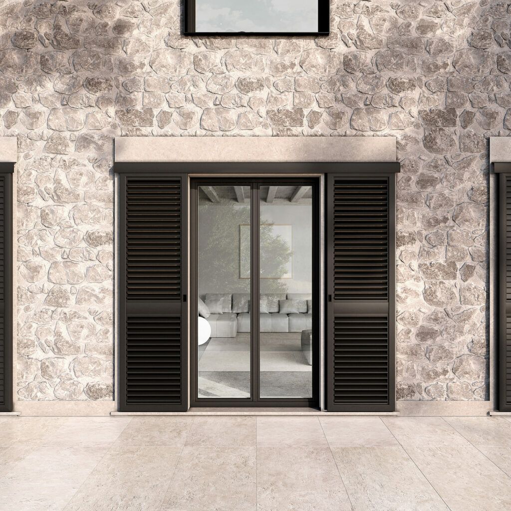 Esterno di un edificio con muri in pietra e persiane scure che incorniciano le porte in vetro.